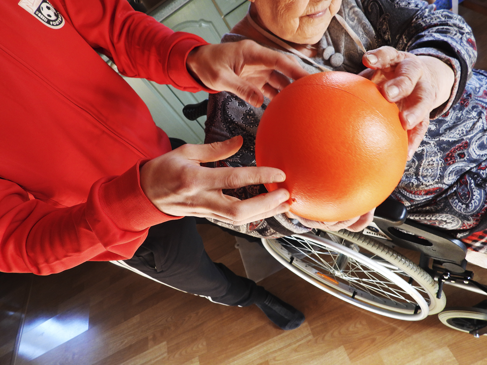 Liikunnanohjaaja ojentaa pallon pyörätuolissa istuvalle