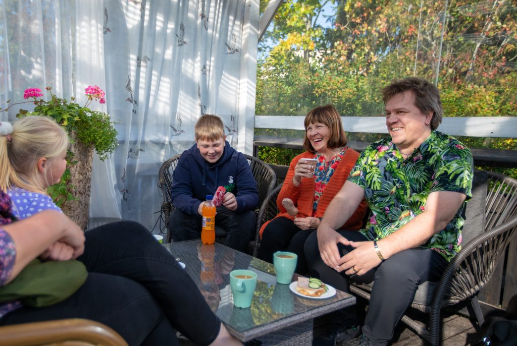Isovanhemmat, vanhemmat ja lapsenlapset kahvilla lasiterassilla.