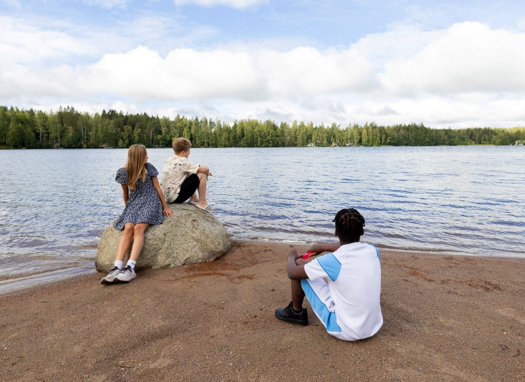 Kolme nuorta istuu rannalla katsomassa järvelle.