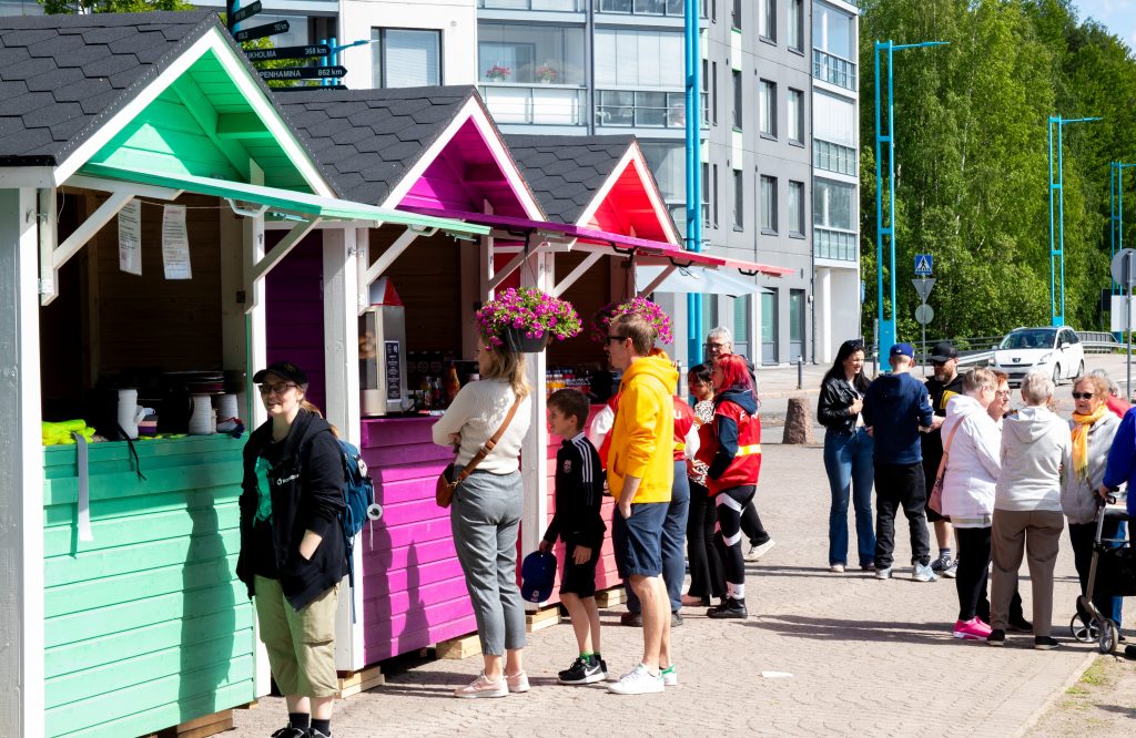 Kolme värikästä kioskia vihreä, pinkki ja punainen, Nummelan keskustassa, joihin jonottaa ihmisiä.